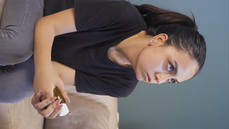 Vertical-video-of-The-young-woman-who-looks-at-the-pills-in-her-hand.